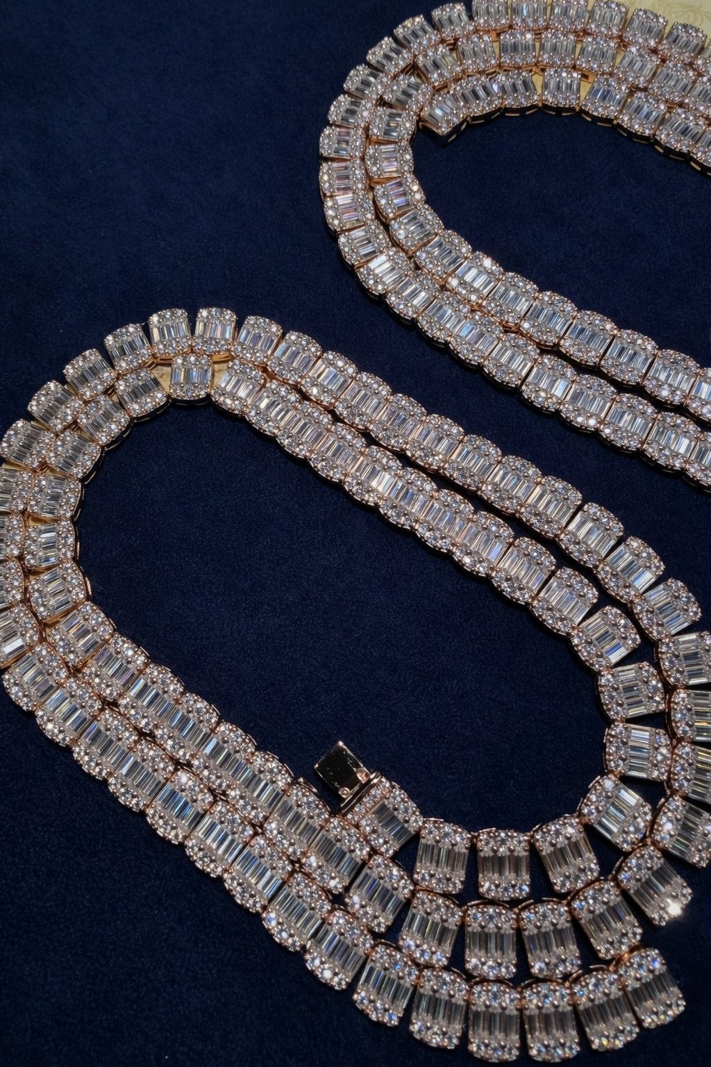Custom iced baguette tennis chain laid on navy velvet, graduated links and fold-over box clasp shown