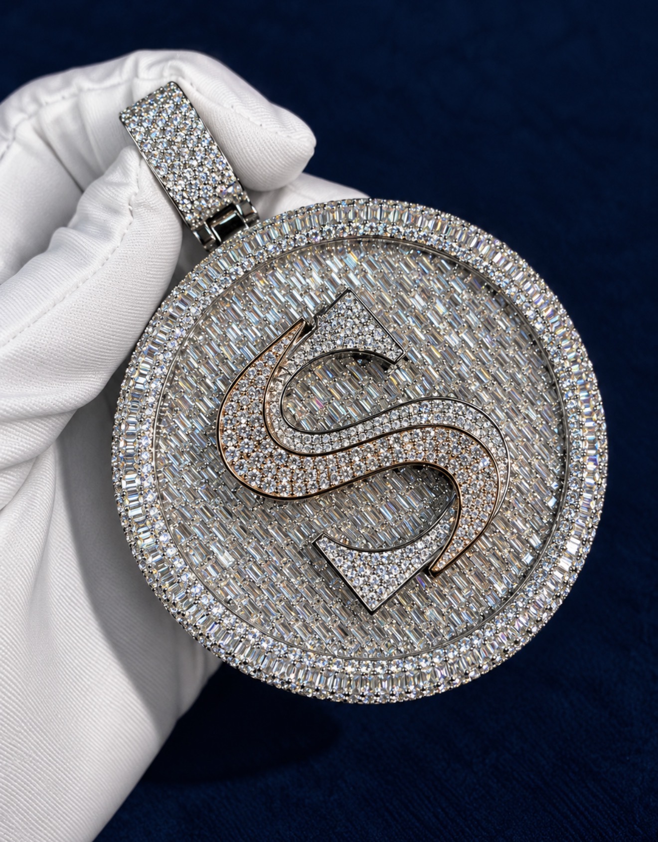 Custom circular medallion pendant fully iced with moissanite, raised monogram in the centre, held in a white glove against a navy background