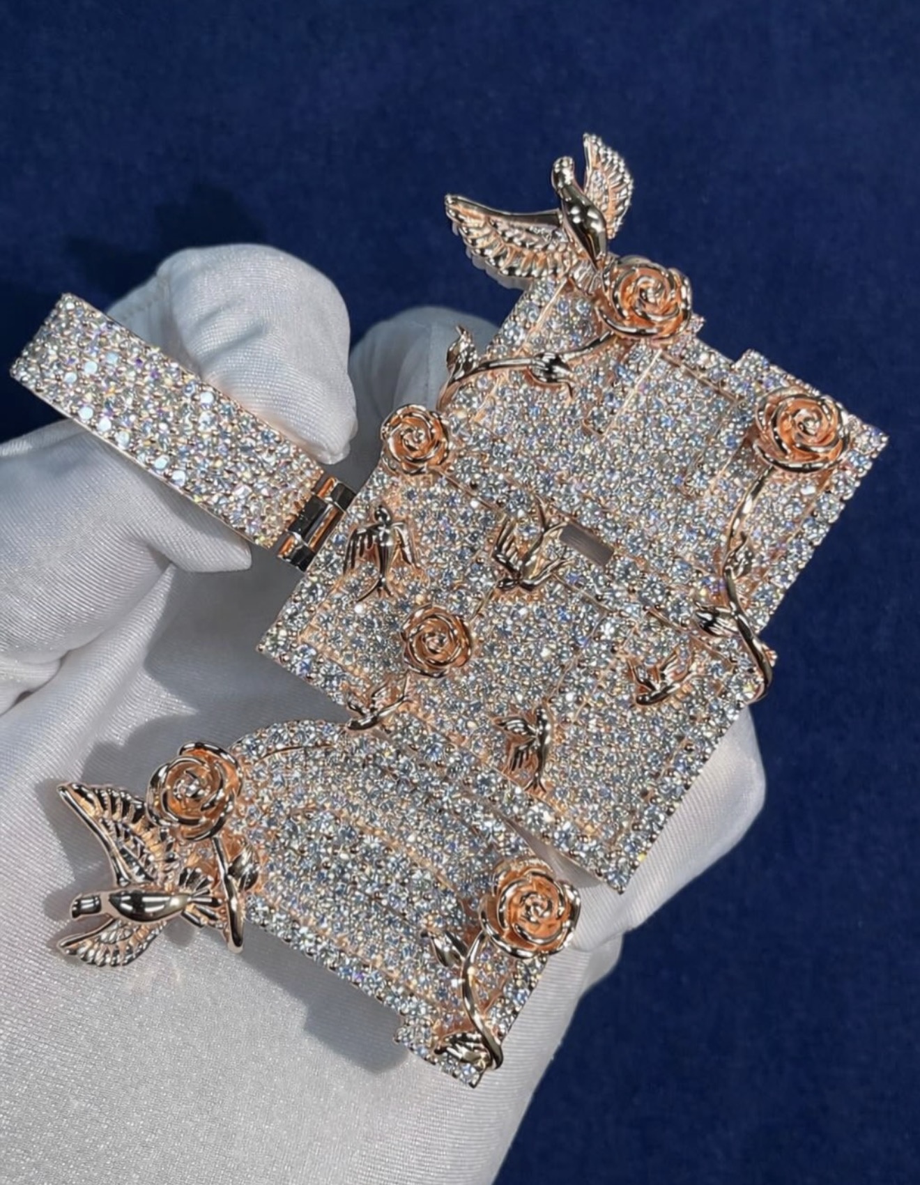 Custom rose and dove pendant fully iced with moissanite, held in a white glove against a navy background