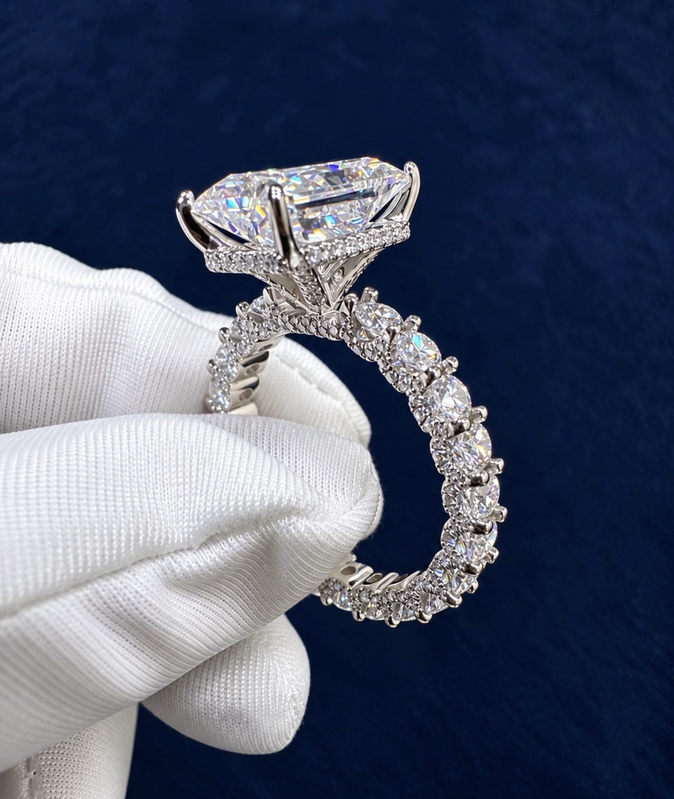 Custom radiant solitaire ring held in a white glove, large moissanite stone over a hidden halo
